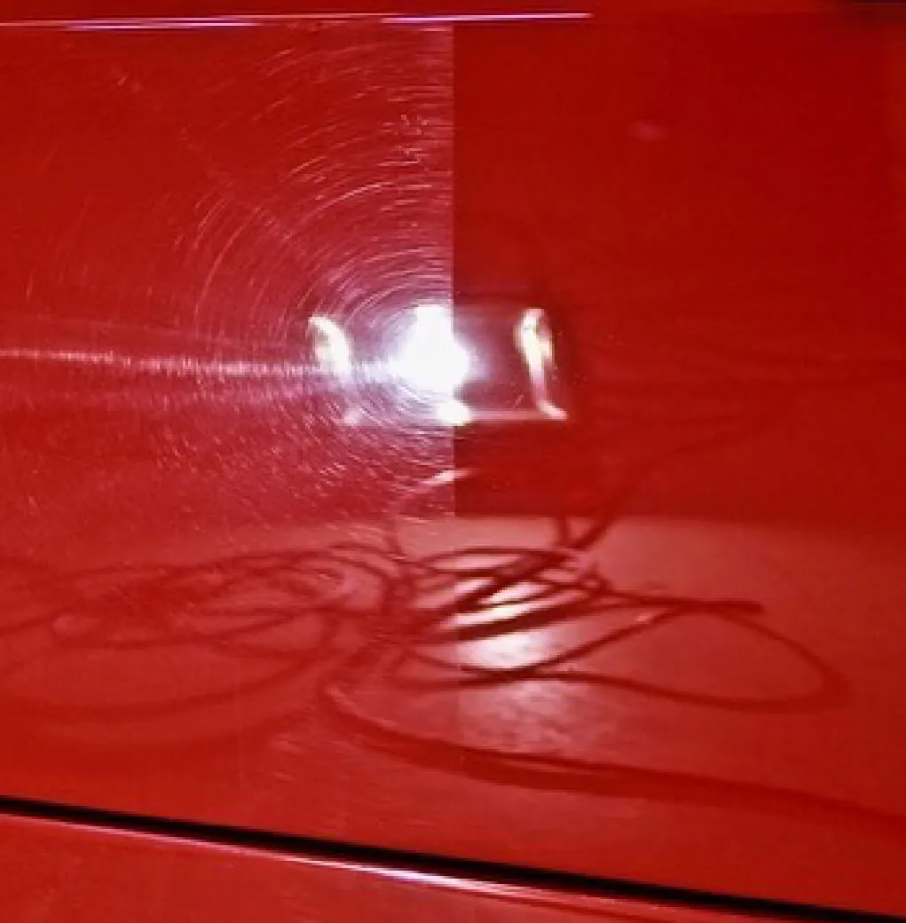 Swirl marks lit up by a light on red paint