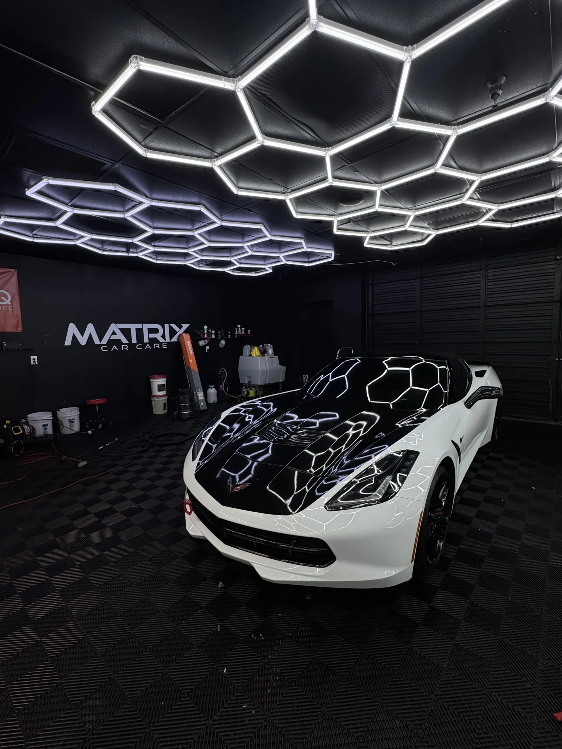 A white Corvette under the studio’s hexagon lights, the Matrix Car Care sign on the wall